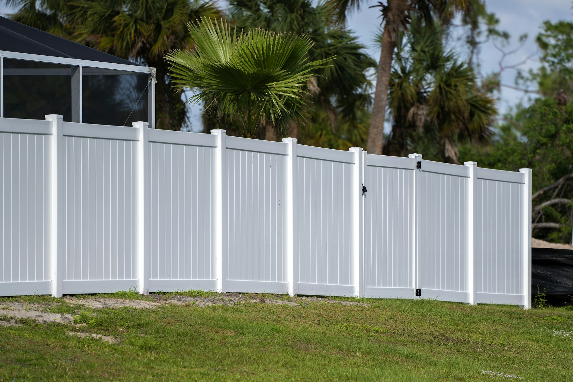 White vinyl picket fence on green lawn surrounding property grounds for backyard